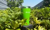 Green Olight insulated travel mug with red splash pattern displayed outdoors in lush green garden bushes