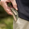 Man's hand inserting olive green EDC knife in pants pocket.