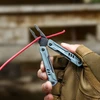 Gloved hand using NexTool multitool pliers to cut a red wire outdoors