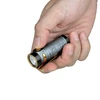 Olight Baton 4/Baton 4 Premium in-hand, with a textured gray body, gold accents, and pocket clip for everyday carry.