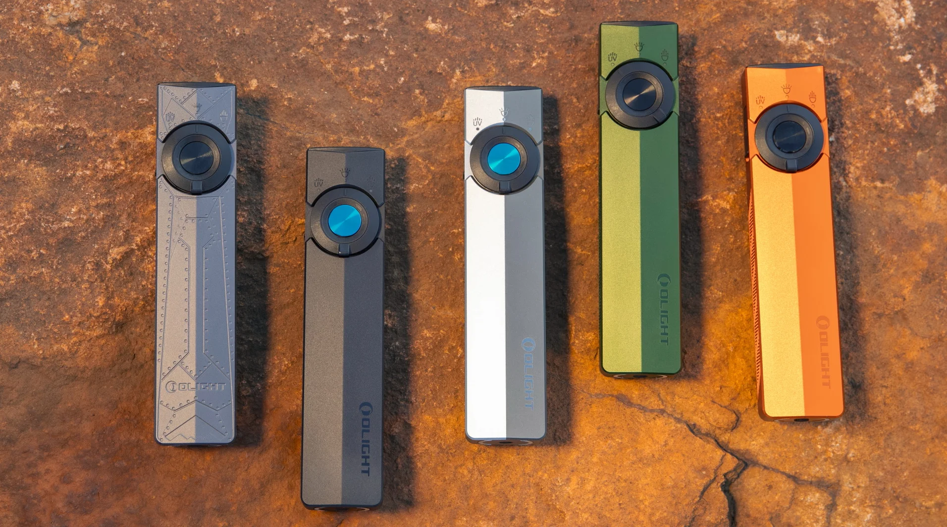 Olight Arkfeld flat EDC flashlights in multiple colors: grey, black, silver, green, orange on a rock.