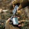 Gloved hands using NexTool multi-tool screwdriver attachment to unscrew keychain accessory outdoors